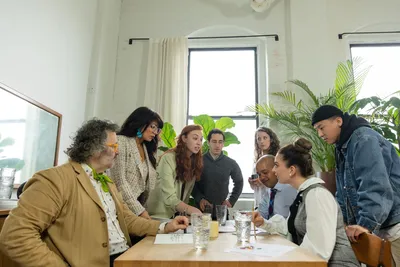 A diverse team discussing ideas at a modern office table with plants and natural light.