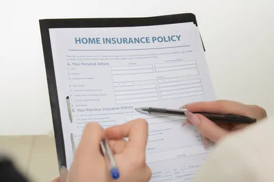 Hands holding pens filling out a home insurance policy document for coverage details.