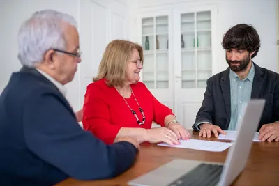 Three business professionals in a meeting, discussing documents and planning strategies indoors.